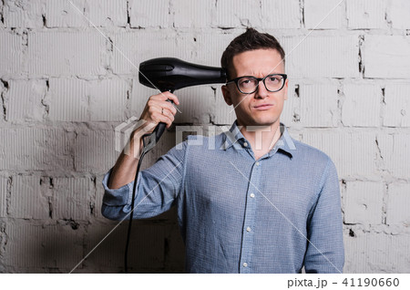 Young crazy stylish man with hairdraier and funny expressions on grey brick wall 41190660
