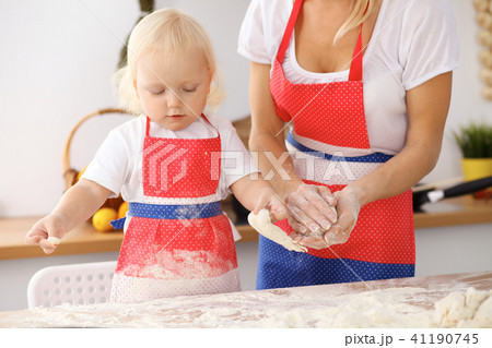 Little girl and her blonde mom in red aprons  playing and laughing while kneading the dough in th 41190745