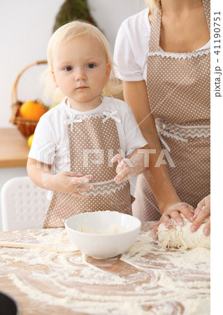 Little girl and her blonde mom in beige aprons playing and laughing while kneading the dough in th Little girl and her blonde mom in beige aprons playing and laughing while kneading the dough in th 41190751