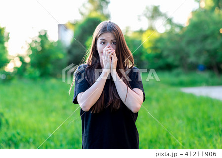 A brunette girl with long summer hair in nature in black T-shirt. Hands covering his mouth 41211906