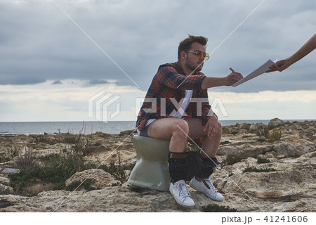 Serious man having seat on toilet near sea Serious man having seat on toilet near sea 41241606