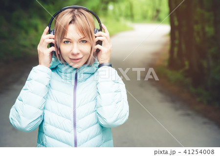 Portrait of an attractive sports girl blonde in a light running down jacket dressing bluetooth 41254008
