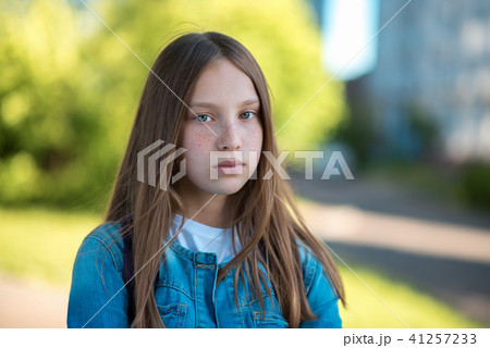 Teenage girl with beautiful long hair. Freckles on the face. Poses on the camera stares. In the 41257233