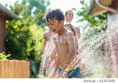 Boy cooling down with garden hose, family in the background 41261888