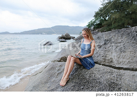Young woman working with laptop on sea shore and sitting on stone. Young woman working with laptop on sea shore and sitting on stone. 41263817