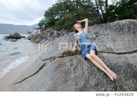 Young caucasian woman lying on stones on sea shore in morning, wearing jeans sundress. Young caucasian woman lying on stones on sea shore in morning, wearing jeans sundress. 41263820