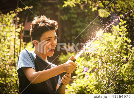 kid hands hold hose with squirting water on the summer sunny green garden 41264976