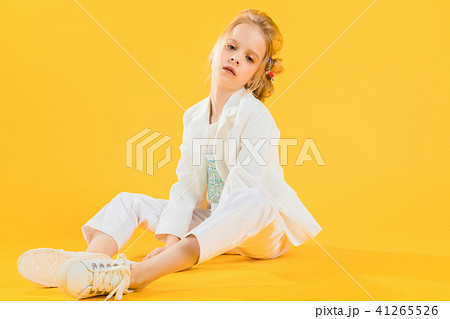 A teenage girl in white clothes sits stretching her legs forward on a yellow background. A teenage girl in white clothes sits stretching her legs forward on a yellow background. 41265526