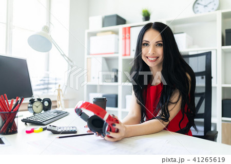 Beautiful young girl with headphones in hands is sitting in the office at the table. Beautiful young girl with headphones in hands is sitting in the office at the table. 41265619