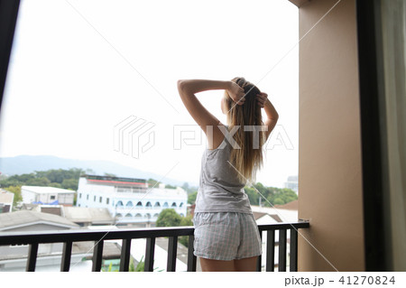 Young european girl wearing summer pajamas standing on balcony and looking at buildings in 41270824