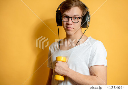 man in headphones holding yellow dumbbel on the yellow background 41284044