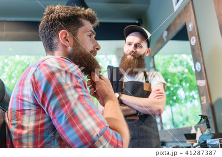 Bearded young man thinking of a trendy change of look in the hair salon Bearded young man thinking of a trendy change of look in the hair salon 41287387