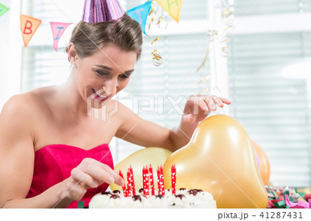 Portrait of a beautiful woman smiling while putting red candles on a cake 41287431