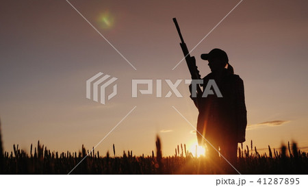 Silhouette of a woman with a gun in her hands. Hunter in the field at sunset 41287895