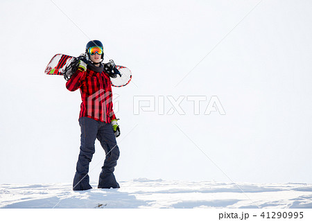 Photo of man with snowboard on shoulders standing on snowy mountainside 41290995