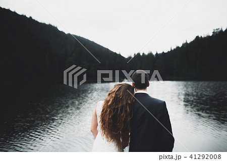 Young newly wed couple, bride and groom kissing, hugging on perfect view of mountains, blue sky Young newly wed couple, bride and groom kissing, hugging on perfect view of mountains, blue sky 41292008