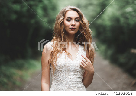 Beautiful bride in elegant white dress holding bouquet posing in park Beautiful bride in elegant white dress holding bouquet posing in park 41292018