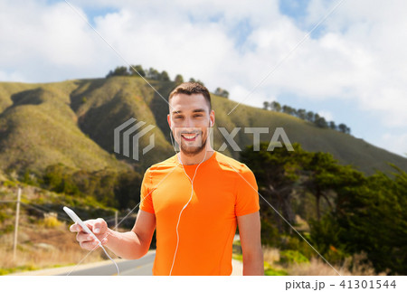 man with smartphone and earphones over hills 41301544