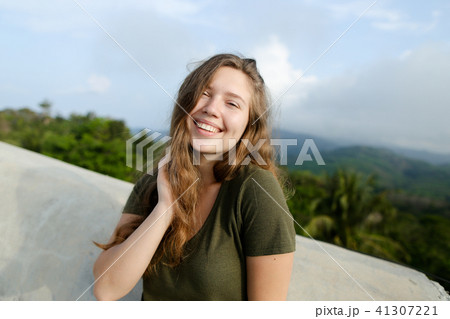Young smiling woman standing in mountains background, wearing khaki shirt. 41307221