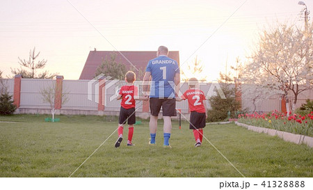 Backshot of grandfather is handling his grandsons, wearing football uniform, with soccerball 41328888