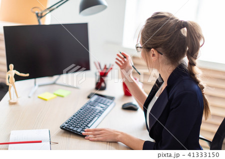 A young girl is sitting at a table, holding a pencil in her hand and working on the computer. A young girl is sitting at a table, holding a pencil in her hand and working on the computer. 41333150