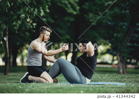 Trainer assisting overweight woman doing sit-ups 41344342