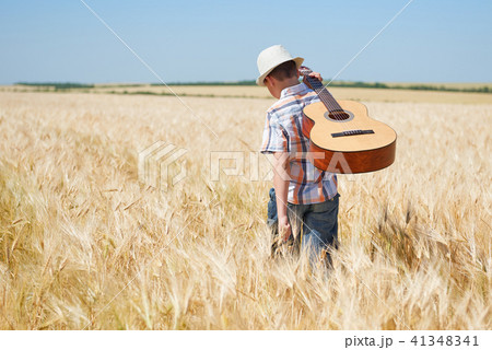 child boy with guitar is in the yellow wheat field 41348341