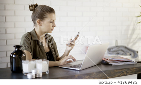 A young girl is holding a phone working with a laptop 41369435