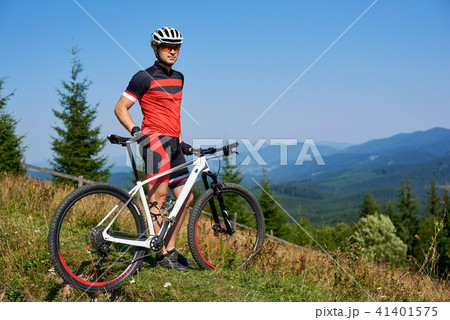 Full length portrait of athletic professional cyclist standing on top of hill Full length portrait of athletic professional cyclist standing on top of hill 41401575