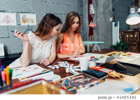 Designers workspace. Two female artists drawing decorative elements sitting at desk in creative Designers workspace. Two female artists drawing decorative elements sitting at desk in creative 41405392