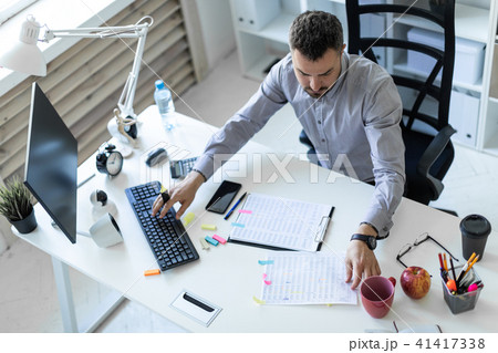 A young man in the office sits at a table, holds a marker in his hand and works with documents and a 41417338