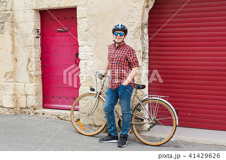 Young man at helmet, sunglasses and red shirt hold bicycle on the backgound red outdoor 41429626