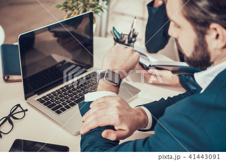 Worker looking at watch at desk in office. 41443091