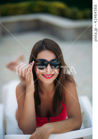 Beautiful lady in sunglasses lies on a longer in front of the pool 41464568