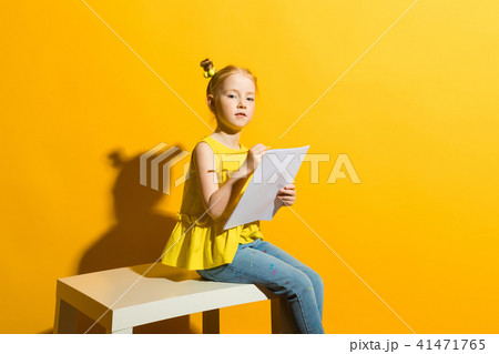 Girl with red hair on a yellow background. Beautiful girl is sitting on the table and is holding a Girl with red hair on a yellow background. Beautiful girl is sitting on the table and is holding a 41471765