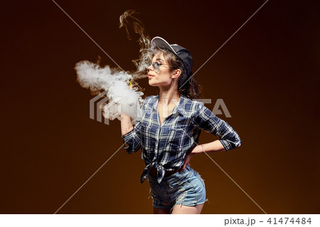 Woman standing and vaping in studio Woman standing and vaping in studio 41474484