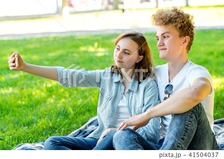 With a girl in the summer in nature. They sit on a blanket. He takes pictures of himself on the 41504037