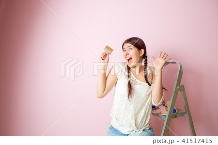 Photo of cheerful woman with brush next to stepladder and roller against blank pink wall. Photo of cheerful woman with brush next to stepladder and roller against blank pink wall. 41517415