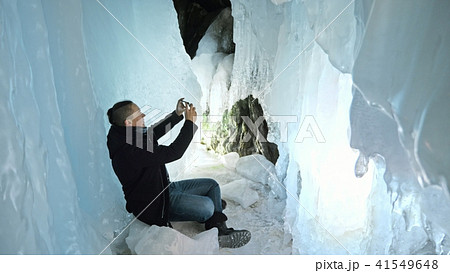 Man communicates in smartphone in an ice cave. Around mysterious beautiful ice grotto. User 41549648