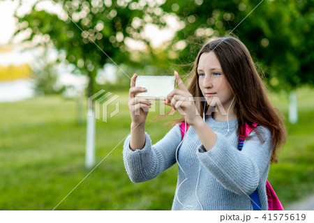 Beautiful schoolgirl girl. In the summer in park in nature. In his hands holds a smartphone. Take 41575619