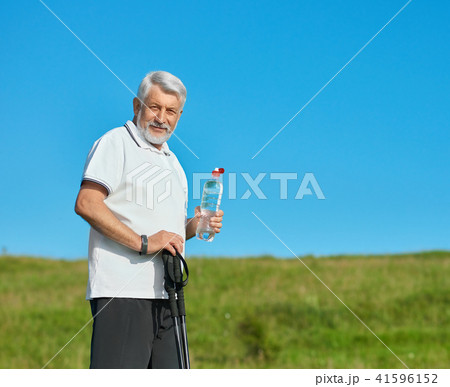 Old man keeping water bottle and tracking sticks. Old man keeping water bottle and tracking sticks. 41596152