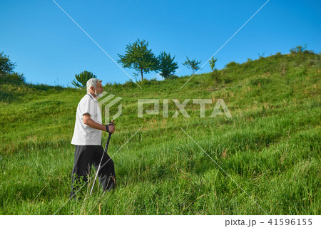 Sideview of old man walking with tracking sticks in mountains. Sideview of old man walking with tracking sticks in mountains. 41596155