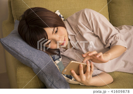 寝転んでスマホを見る若い女性の写真素材