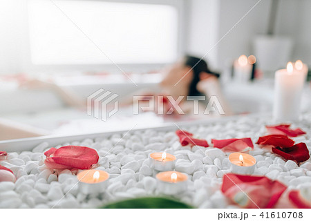 Woman lying in bath, rose petals, burning candles 41610708
