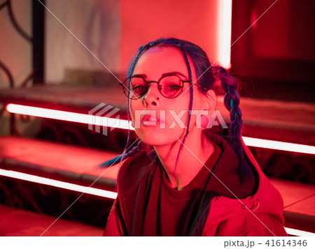 Young pretty girl with unusual hairstyle sitting on stairs which glowing red neon lights. City at 41614346