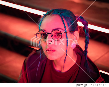 Young pretty girl with unusual hairstyle sitting on stairs which glowing red neon lights. City at 41614348