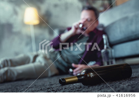 Bottle of cognac lying on the floor near drunk man 41616956