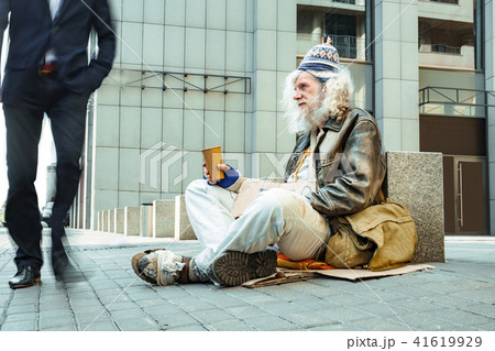 Poor starving man in tattered clothes sitting outside 41619929