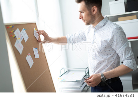 A young man stands near a board with stickers and holds a pen in his hand. A young man tears off a A young man stands near a board with stickers and holds a pen in his hand. A young man tears off a 41634531