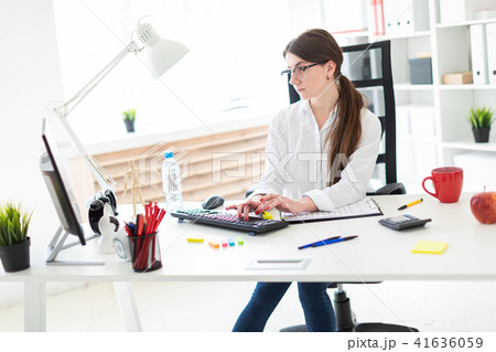 A young girl is sitting at a table in the office and typing on the keyboard. 41636059